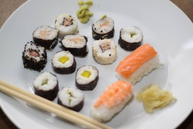 Farklı suşi türlerinin yakın çekimi, yemek çubuklarıyla beyaz bir tabakta servis edilir.,