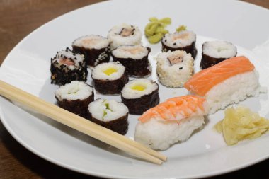 Farklı suşi türlerinin yakın çekimi, yemek çubuklarıyla beyaz bir tabakta servis edilir.,