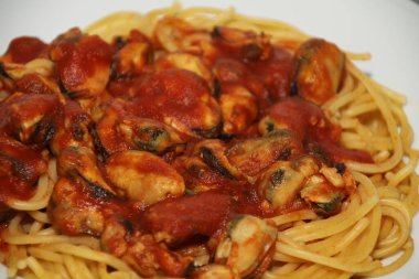 Beyaz bir tabakta servis edilen midyeli, domates soslu spagetti.,