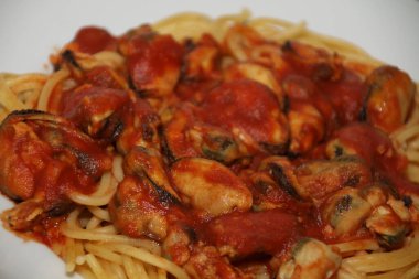 Beyaz bir tabakta servis edilen midyeli, domates soslu spagetti.,