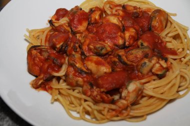 Beyaz bir tabakta servis edilen midyeli, domates soslu spagetti.,