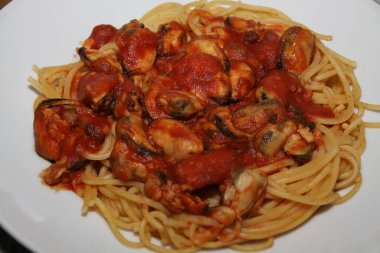 Beyaz bir tabakta servis edilen midyeli, domates soslu spagetti.,