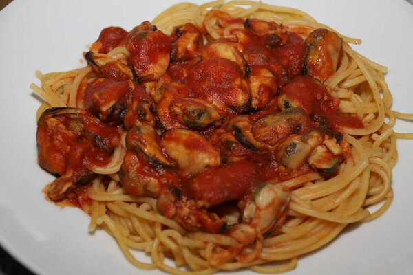 крупным планом спагетти с мидиями, томатным соусом, подается на белой тарелке,