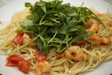 Beyaz bir tabakta servis edilen karidesli, domatesli ve rikoalı makarna.,