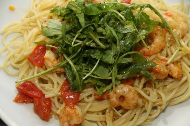 Beyaz bir tabakta servis edilen karidesli, domatesli ve rikoalı makarna.,