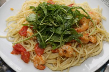 Beyaz bir tabakta servis edilen karidesli, domatesli ve rikoalı makarna.,