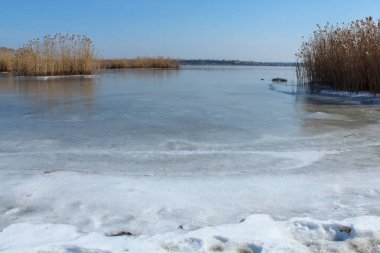 Güneşli bir günde karla kaplı donmuş bir nehrin manzarası.