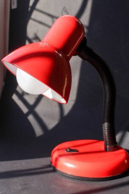 Siyah arka planda kırmızı bir masa lambası var.