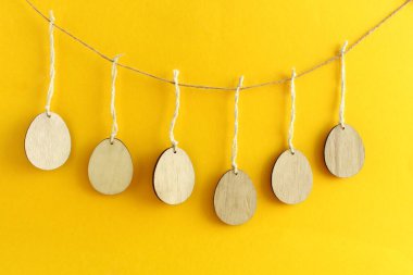 Ahşap Paskalya yumurtaları sarı arka planda ipte sallanıyor.