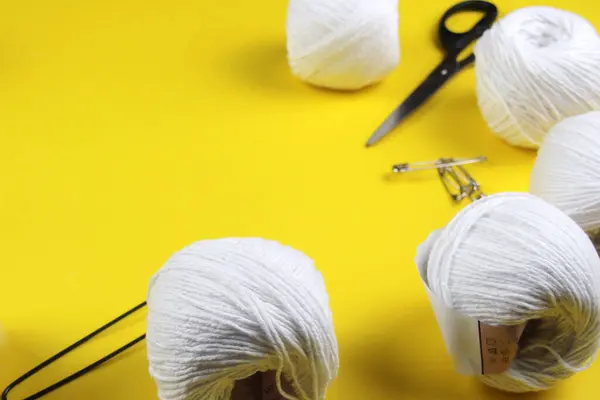 Sarı arka planda, bir makas ve beyaz iplik yakın plan gösterilir