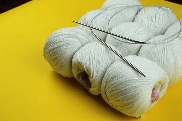Örgü örmek ve örgü örmek için beyaz iplik sarı arka planda yatar. İş konsepti