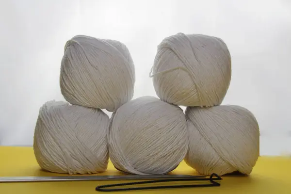 Piramit şeklindeki beyaz iplik beyaz ışıkla aydınlatılır. Örgü aksesuarları yakınlarda yatıyor.