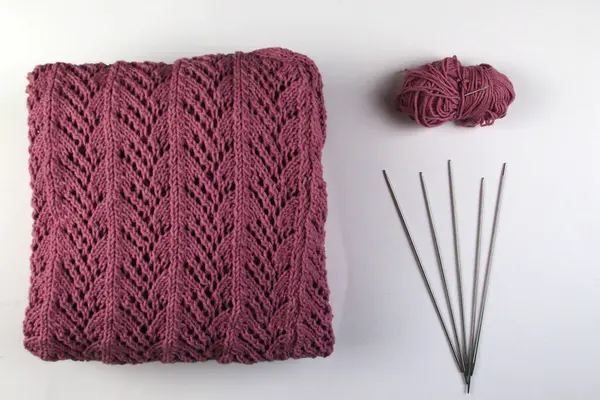 Pembe bir el yapımı süveter beyaz bir arka planda yatar. Örgü iğneleri ve iplik yumağı.
