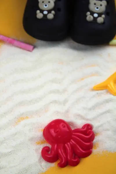 Arka planda kırmızı kum kalıbı, terlikler ve plaj oyuncakları olan dalgalı kum..