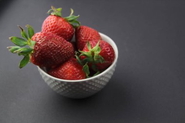 Gri arka planda sulu ve büyük çilek dolu gri bir kase duruyor. Sağlıklı beslenme.