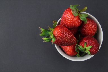 Çilekler siyah arka planda gri bir kasede yatar. Çiftlik yemeği..