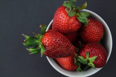 Çilekler siyah arka planda gri bir kasede yatar. Sağlıklı beslenme.