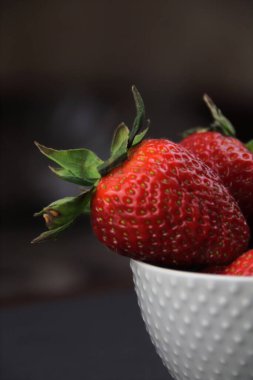 Siyah arka planda gri bir tabakta büyük çilekler var. Çiftlik kavramı, sağlıklı beslenme..