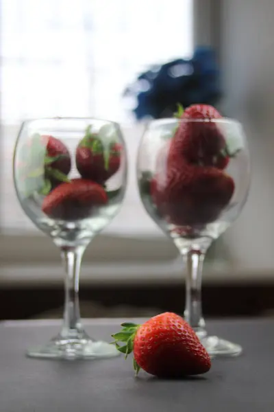 Siyah arka planda çilek dolu bardaklar var, ön planda sulu bir dut var. Sağlıklı beslenme kavramı.