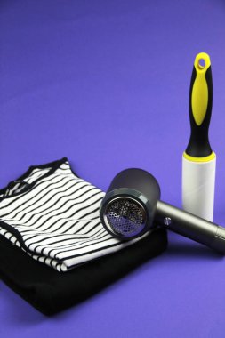 Mor bir arka planın dikey fotoğrafı. Çerçevede katlanmış giysileri görebilirsiniz. Üzerinde bir iplik makinesi var. Arka planda ise bir kıyafet destekleyici var.