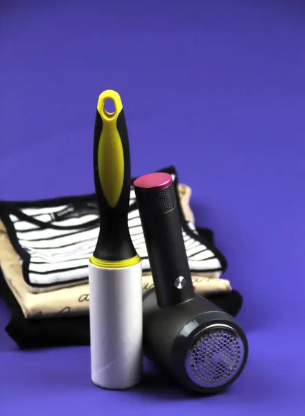 Bir giysi silindiri ve iplik çıkarma makinesi mor arka planda duruyor. Arka planda farklı renklerde birkaç tişört var..