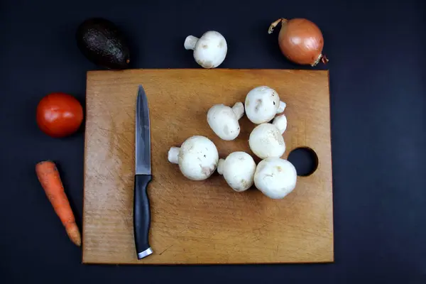 Sağlıklı yemek yeme kavramı. Tahtada bir bıçak ve bir mantar piramidi var, tahtanın çevresinde sebzeler var.
