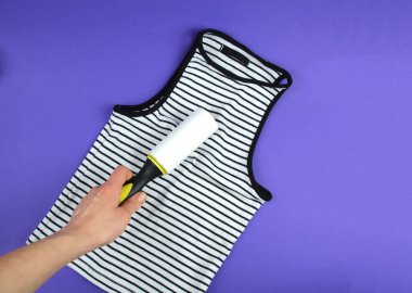 Kadının eli, tişörtünü temiz tutmak için giysi silindiri kullanıyor.