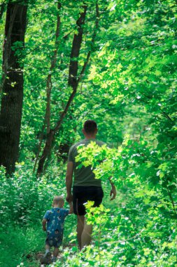 Baba ve oğul ormanda el ele yürüyorlar.