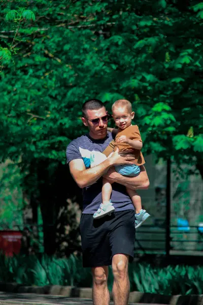 Babam bir yaz günü parkta bebeğini kollarında taşıyor.