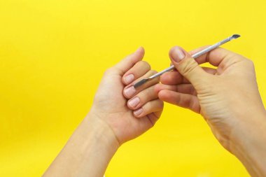 Kadın elleri evde manikür yapıyor. Bir spatula kullanarak, tırnak etlerini çıkarıyorlar.