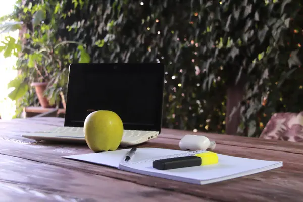 Dizüstü bilgisayar, bir not defteri, bir kalem ve ön planda parlak yeşil bir kalemle ahşap bir masanın üzerinde duruyor..