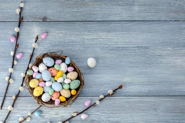 Colorful chocolate Easter eggs in a nest on the table, next to willow branches