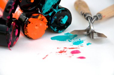 Beyaz tuval üzerinde Renkli Kırmızı, Turuncu ve Turkuaz Boya Tüpleri ve Spatula