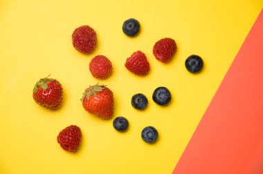 Taze yaban mersini, çilek ve ahududu. Sarı arka planda.