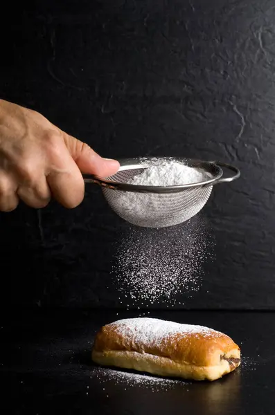 Person Adding Powdered Sugar To a Chocolat Pastry using a Stainless Steel Strainer on Black Background Vertical