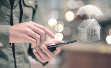 Kanaldaki ev bir şemsiye tarafından korunuyor. Sanal sigorta kavramı. Elinde telefon tutan bir adam.