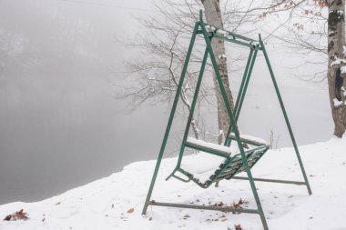 Parktaki bankta kışın karla kaplı.