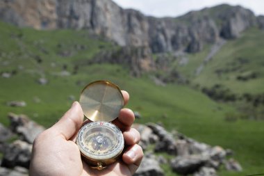 Dağların arka planında altın bir pusula tutan el.