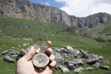 Dağların arka planında altın bir pusula tutan el.