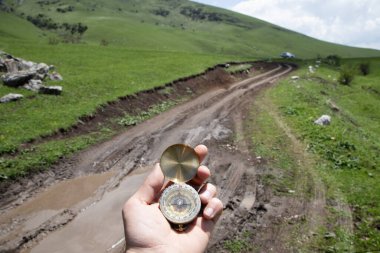 Dağlardaki bir yolun arka planında bir pusula tutuyor