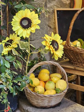 Dışarıda sepetin içinde güzel ayçiçekleri ve limonlar var. Dikey fotoğraf.
