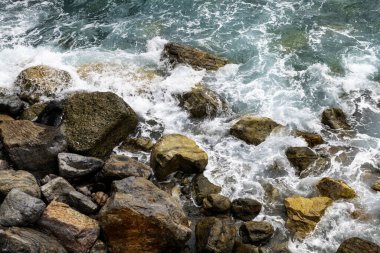 Dalgalar ve turkuaz okyanus dalgaları engebeli kayaların üzerinde yuvarlanıyor..