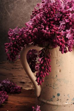 Eski aşınmış seramik sürahide mor leylakların dikey fotoğrafı. Sürahi sapı ve leylak çiçeklerinin yakın çekimi.