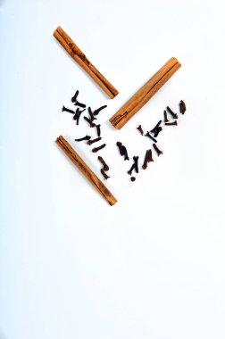 Beyaz yüzeyde karanfil ve tarçın çubukları var. Görüntünün alt kısmında fotokopi alanı ile yüksek açılı çekim. Dikey fotoğraf.