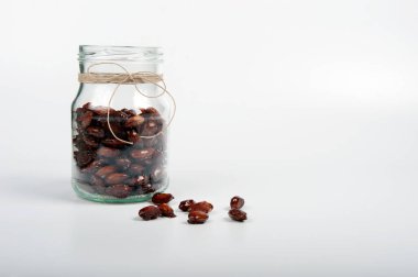 Kavanozu yanık bademlerle açın. Resmin sağ tarafında kopyalama alanı olan beyaz arkaplan. Etrafa çok az badem yayılır. Cam kavanozda jöleli badem ve fiyonkta doğal ip..  