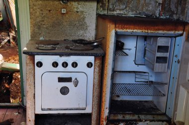 Harap olmuş kır evinde terk edilmiş bir ocak ve buzdolabı. Paslanma ve çürüme..