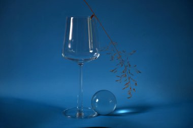 Boş bardak, cam top ve mavi arka planda kurumuş saman.