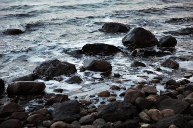 Plajda ıslak taşlar ve çakıl taşları. Okyanustan köpük ve dalgalar. Yatay fotoğraf.