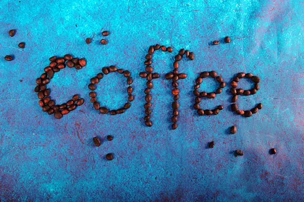 stock image Coffee beans arranged to spell the word coffee on blue turquoise background. A cool posster for the kitchen or the coffee shop.