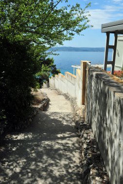 Hırvatistan 'ın Brela plajına giden dar sokak ve merdivenlerin dikey fotoğrafı.